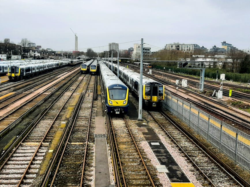 Multiple modern passenger trains parked on railway tracks near South Harrow station, with some trains featuring a yellow and grey color scheme. The tracks are made of steel rails and wooden sleepers,